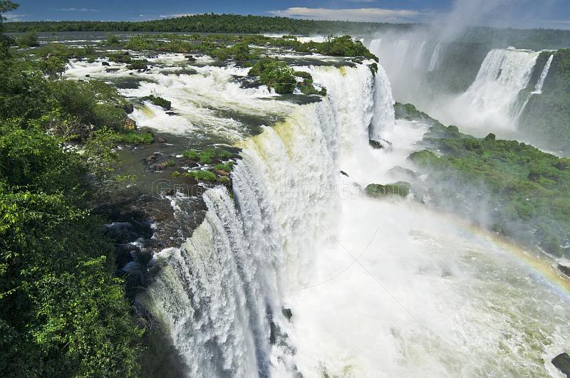 Water with rainbow cascades into the river at the Iguazu Falls.