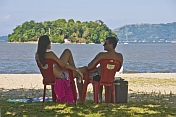 Couple sit on beach looking at island in the Bahia Da Ilha Grande.