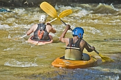 Two canoeists in kayaks negotiate some turbulent water.