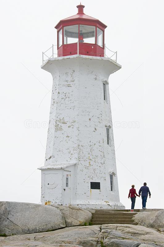 Man and woman walk past Peggy\\'s Cove lighthouse tower.