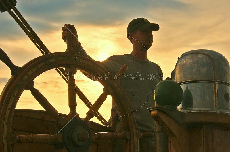 Young trainee seaman takes the wheel of the Barque 'Picton Castle' at sunset.