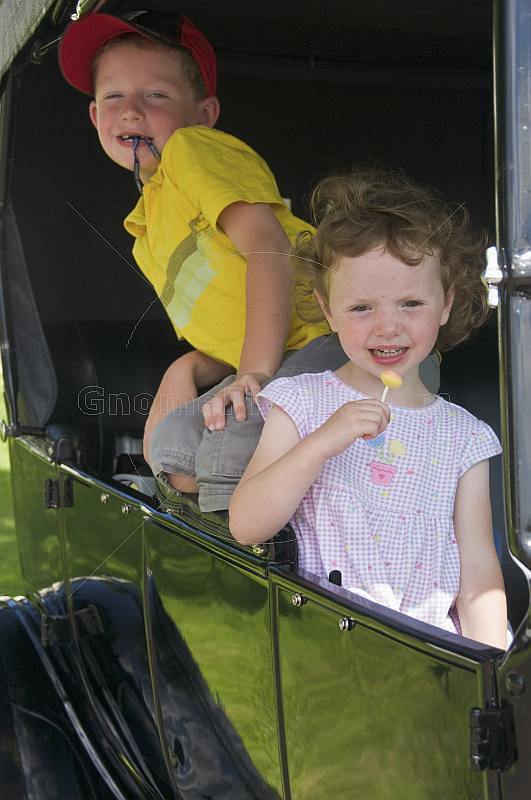 Small girl with lollipop and boy in yellow shirt wait in the back seat of a Model T Ford vintage car.
