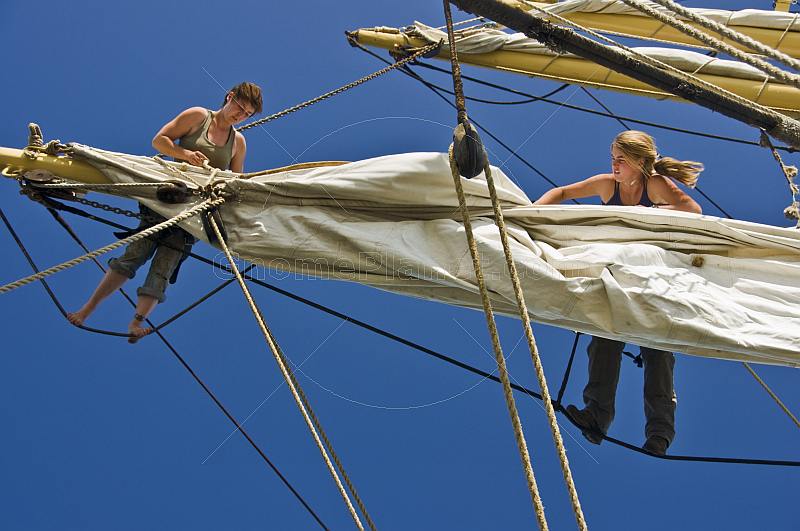 Two women crew members of the tallship 'Picton Castle' work aloft to stow sail.