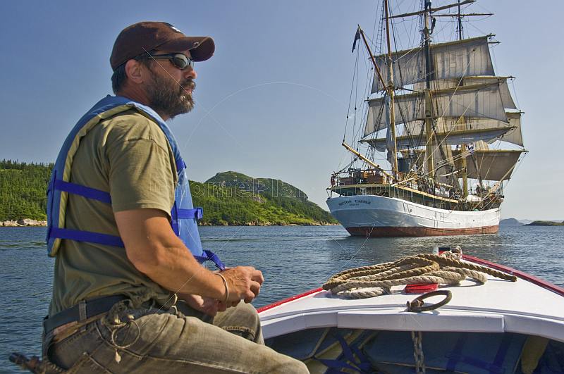 Man in small motor boat watches the square rigger \\'Picton Castle\\' as she sets sail towards the ocean.