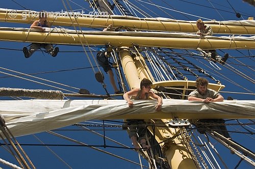 Crew of the tallship 'Picton Castle' work aloft to stow sail.
