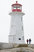 Man and woman walk past Peggy\\'s Cove lighthouse tower.