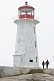 Image of Man and woman walk past Peggy\\\\'s Cove lighthouse tower.