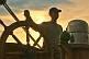 Image of Young trainee seaman takes the wheel of the Barque 'Picton Castle' at sunset.