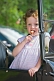 Image of Small girl with lollipop and lilac dress waits in the back of a vintage Model T Ford car.