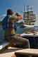 Man in small motor boat takes photo of the tallship 'Picton Castle' as she sets sail towards the ocean.