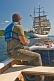 Man in small motor boat watches the square rigger \\'Picton Castle\\' as she sets sail towards the ocean.