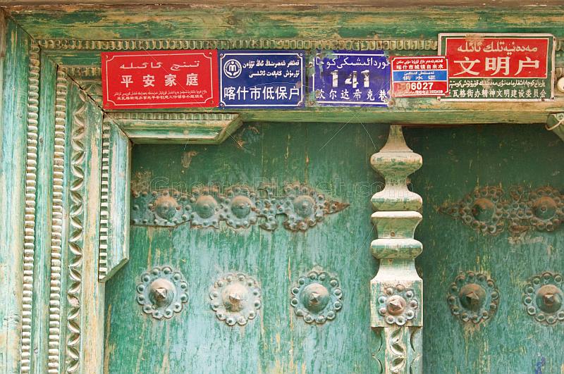Red and blue signs with Chinese and Uighur writing, on a green door.