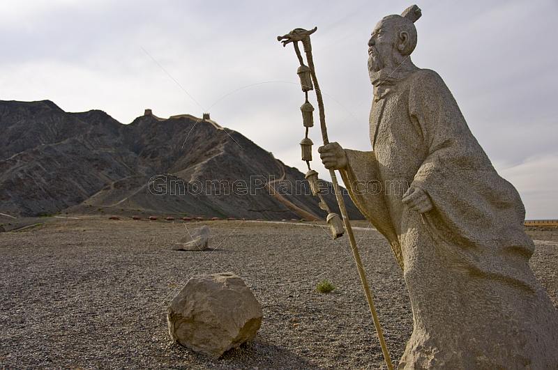 Statue of Chinese wandering monk next to a reconstructed section of the Great Wall of China at the Shiguan Gorge, near Jiayuguan.