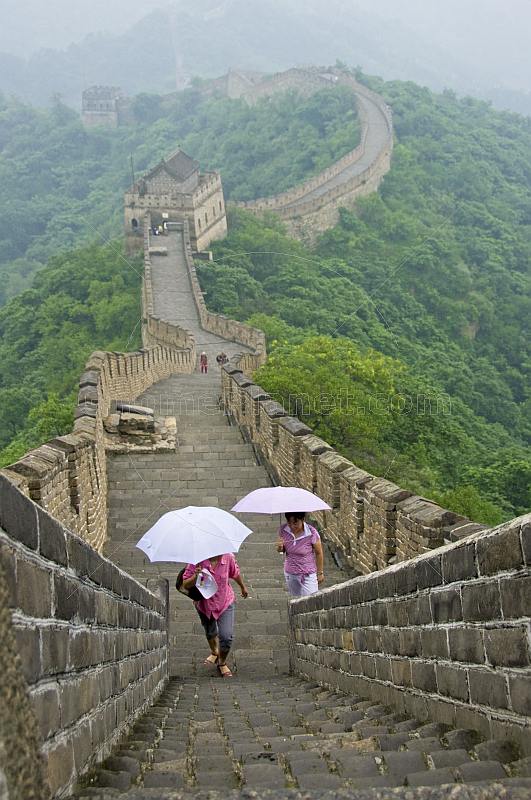Two Chinese ladies with umbrellas walk along the Great Wall of China.
