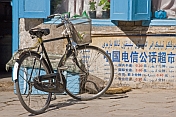 Bicycle parked in the street, next to a wall with Chinese characters.