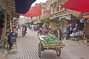 A trader pushes a cart of cucumbers down a busy street in the old city.