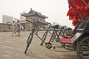 Chinese visitors walk past red and black bicycle rickshaws on the city walls.