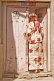 Image of Uighur woman in white and red skirt and top, standing in pink doorway.
