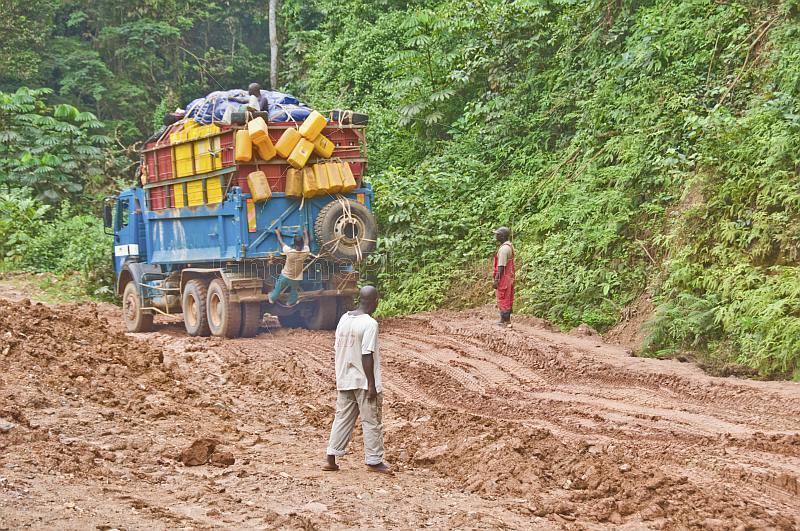 Men watch as heavily laden truck negotiates a muddy section of jungle road.