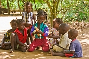Group of children sit in the shade and play with a plastic doll.