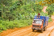 A heavy truck with roof riders drives along a rough and muddy jungle road.