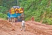 Men watch as heavily laden truck negotiates a muddy section of jungle road.