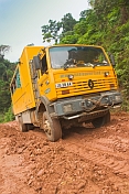 Oasis Overland truck drives through muddy section of jungle logging road.