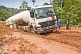 A white fuel tanker struggles to drive along muddy and deeply rutted logging roads.