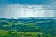 Image of Rain falls from dark clouds over the hills and valleys of forested countryside.