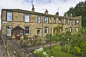 A row of Yorkshire stone terraced cottages with flower gardens.
